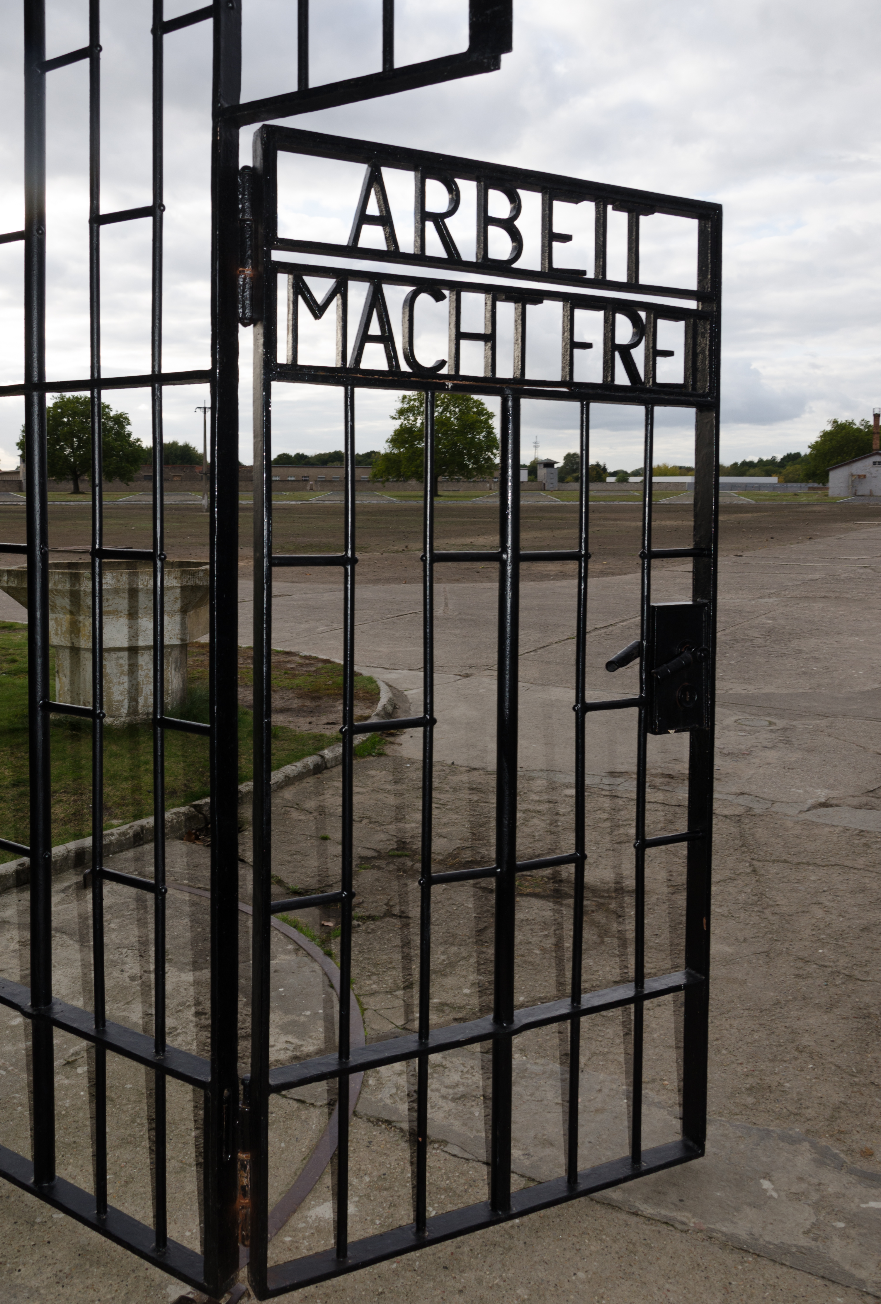 Hedendaagse foto van het toegangshek van concentratiekamp Sachsenhausen. Op het zwarte metalen hek staat de tekst ‘Arbeit macht frei’. 